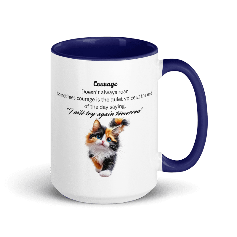 A white ceramic mug with a dark navy blue interior, handle, and rim. The front of the mug features a printed design with the word 'Courage' in black text above a photo of a small calico kitten and a quote.