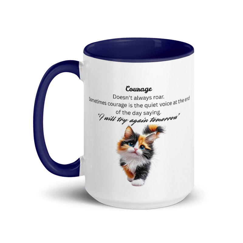 A white ceramic coffee mug with a dark navy blue handle and interior, featuring a printed definition of the word 'Courage' and a cute calico kitten illustration on the front.