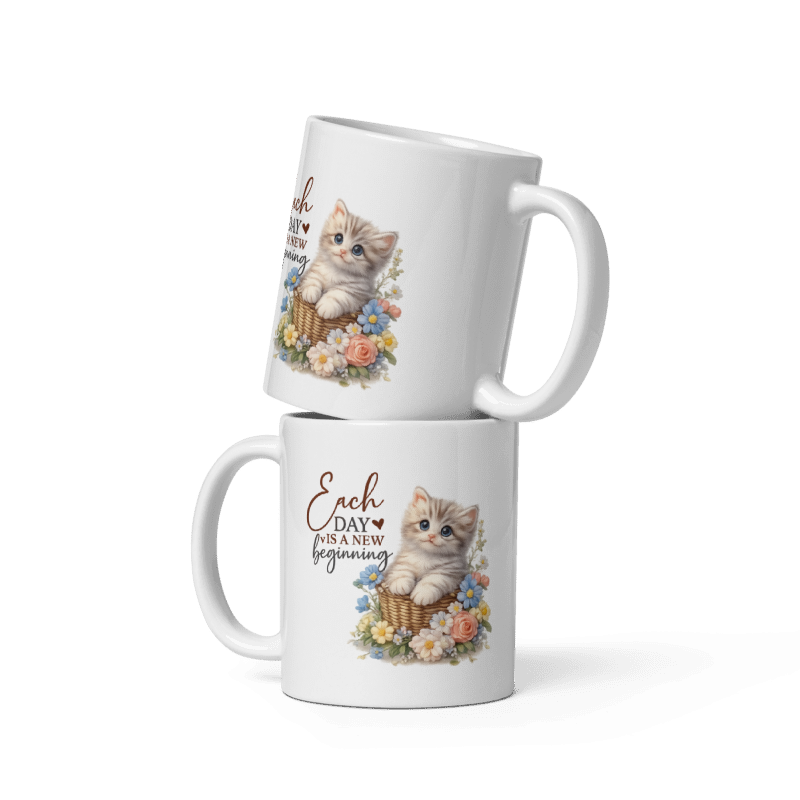 Two stacked white ceramic mugs with a printed design of a kitten in a basket surrounded by flowers and the text 'Each day is a new beginning'.