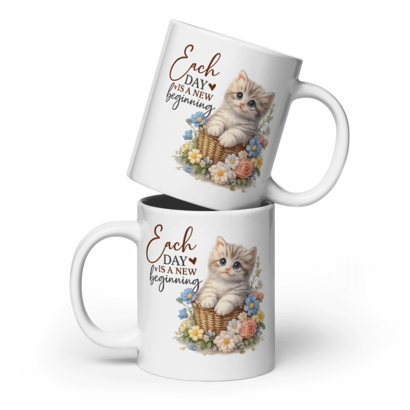 Two white ceramic mugs stacked with a kitten illustration and the printed phrase 'Each day is a new beginning' on a clean white background.