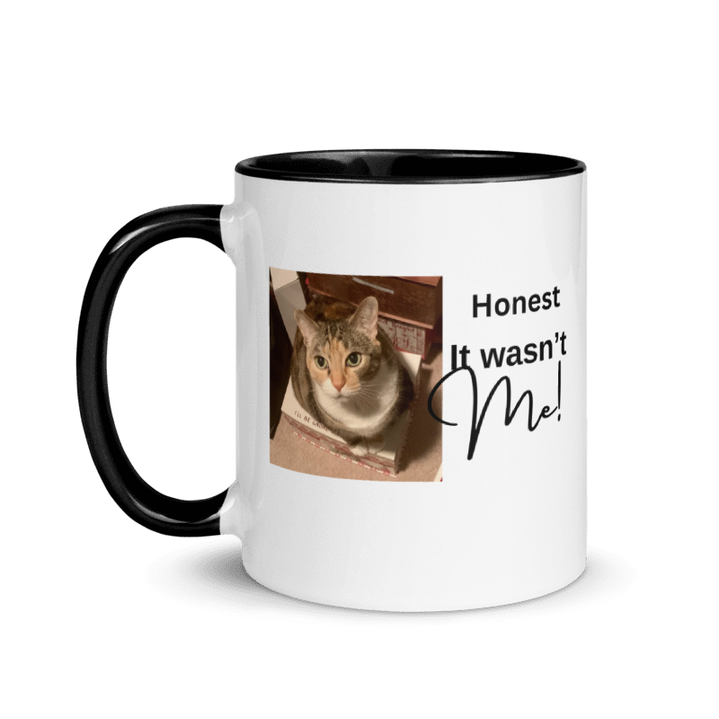 A white ceramic mug with a black handle and black interior, featuring a printed graphic of a cat and the text 'Honest It wasn't Me!' on the side.