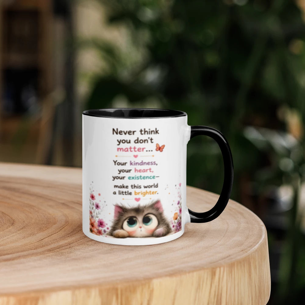A white ceramic mug with a black handle and interior, featuring a printed message and a cute cat illustration, sitting on a round wooden table with a blurred green garden background.