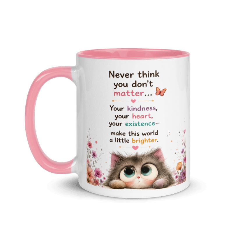 A white ceramic mug with a pink handle and pink interior, featuring a printed quote about kindness and a cute cartoon kitten illustration with floral accents.