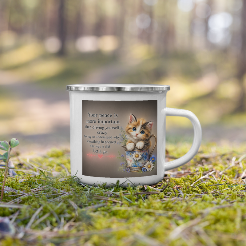 A white enamel-style mug with a silver rim sits on green moss in a blurred outdoor forest setting. The mug features a printed graphic of a small orange tabby kitten sitting in a blue flower pot with daisies, next to a quote that reads, 'Your peace is more important than driving yourself crazy.