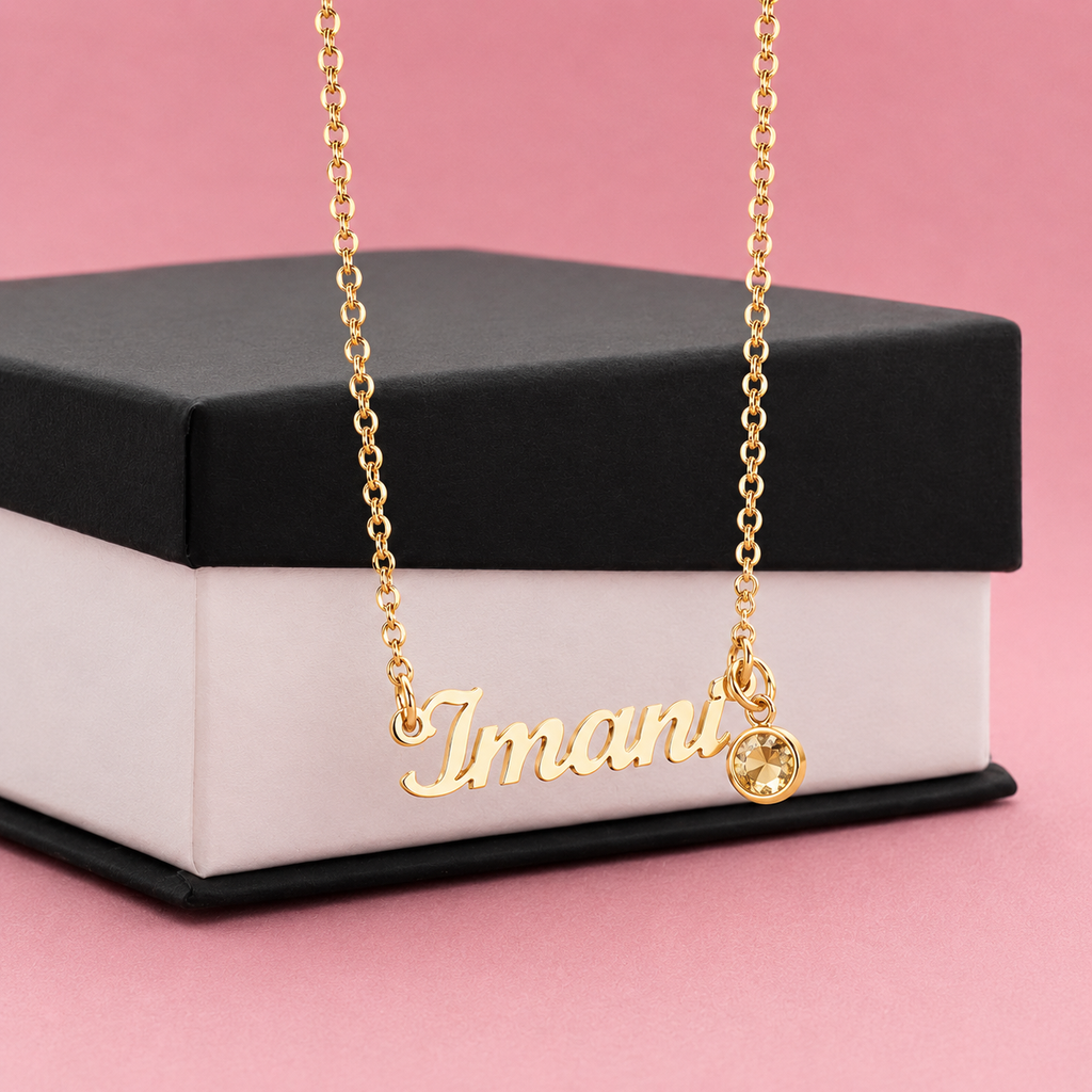 Gold necklace with birthstone pendant on a black and white box with pink background