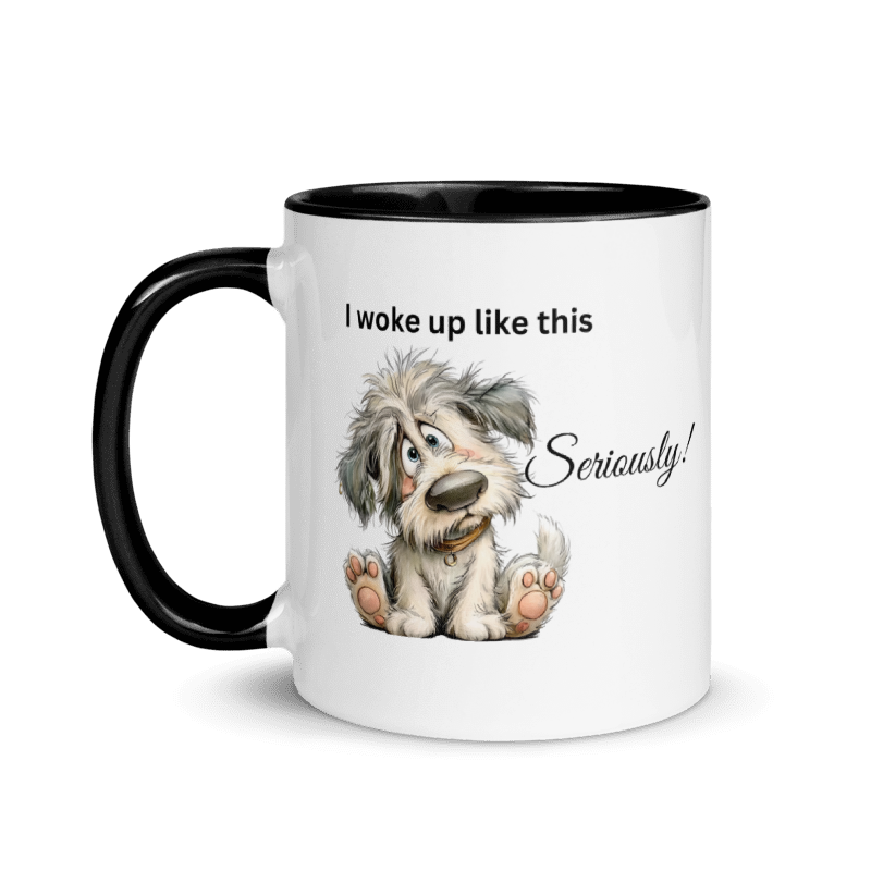 A white ceramic coffee mug with a black handle and black interior, featuring a cartoon illustration of a fluffy gray and white dog sitting down with the text 'I woke up like this Seriously!' 