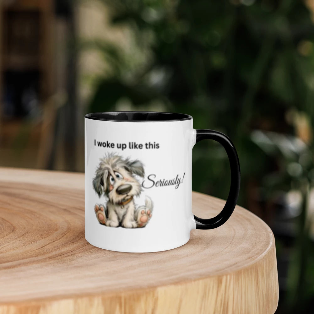 A white ceramic coffee mug with a black handle and interior, featuring a cartoon illustration of a scruffy dog and the text 'I woke up like this Seriously!' on a wooden table with a blurred green garden background.