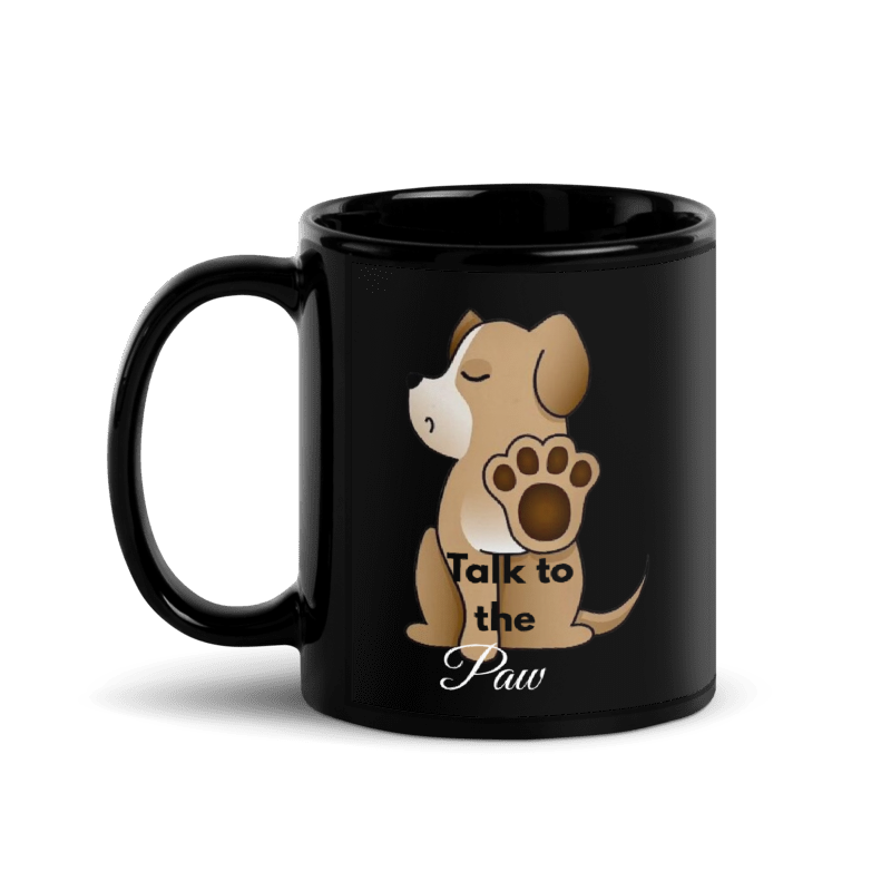 A glossy black ceramic mug featuring a cartoon illustration of a brown puppy sitting with its paw raised, accompanied by the text 'Talk to the Paw'.