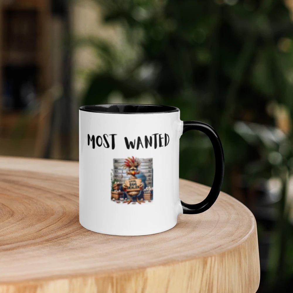Mug with 'MOST WANTED' text and graphic on a wooden surface with blurred greenery in the background