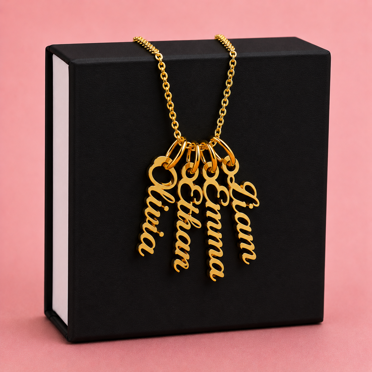 Gold necklace with 4 name pendants on a black box against a pink background