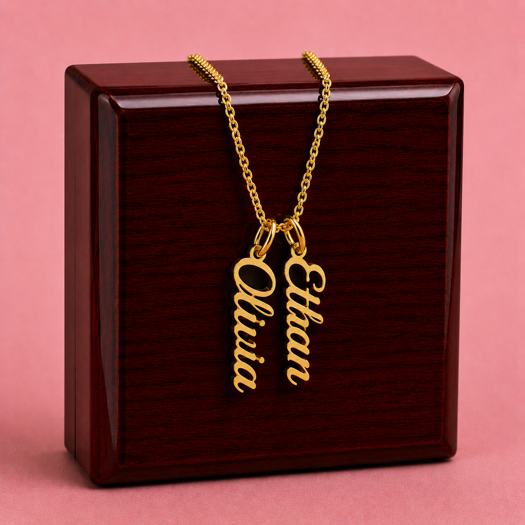 Gold necklace with 'Olivia' and 'Ethan' charms on a wooden box with a pink background
