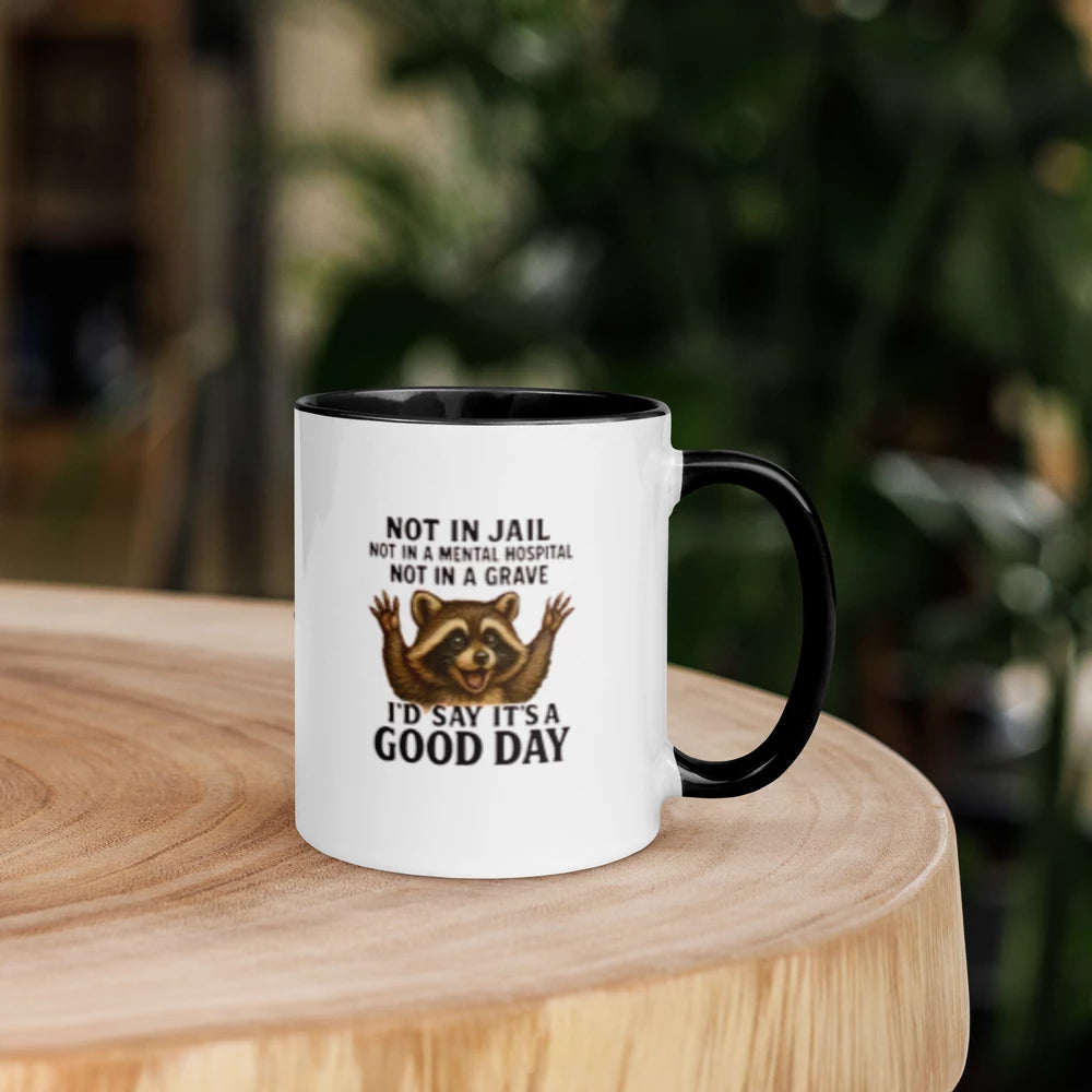 Mug with a raccoon illustration and humorous text on a wooden surface with a blurred background