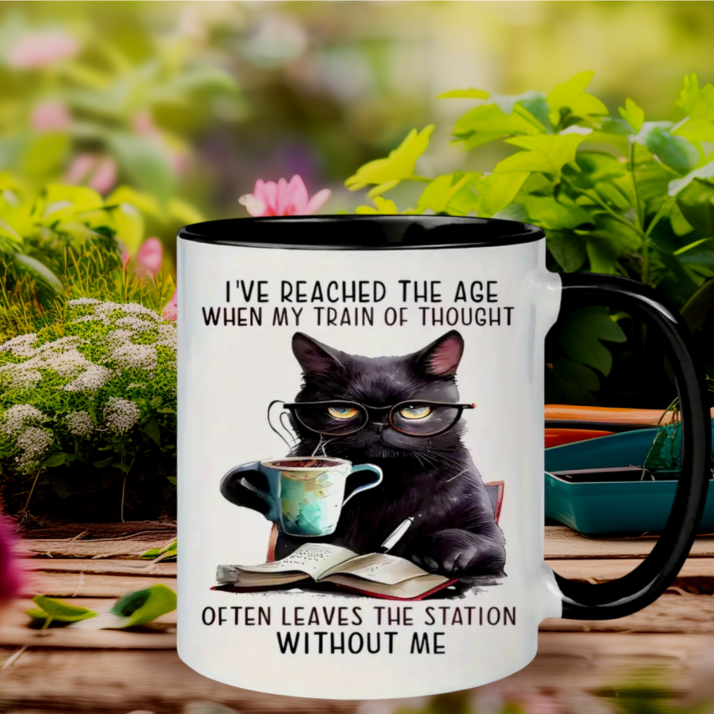 Mug with a black cat wearing glasses, holding a cup, and reading a book with text about a cat's train of thought.
