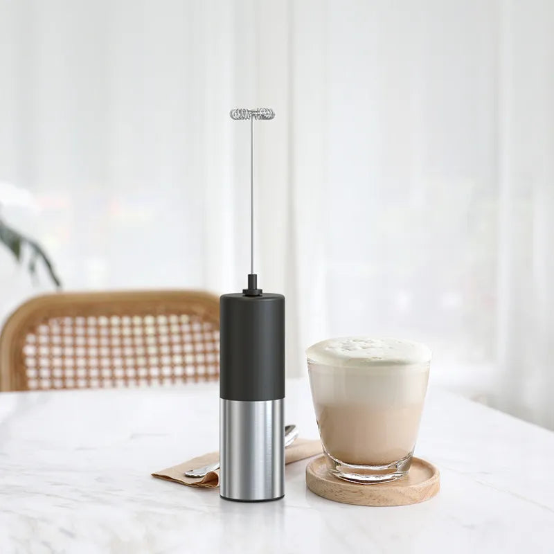 Black and silver frother next to a glass of latte on a white surface with a blurred background
