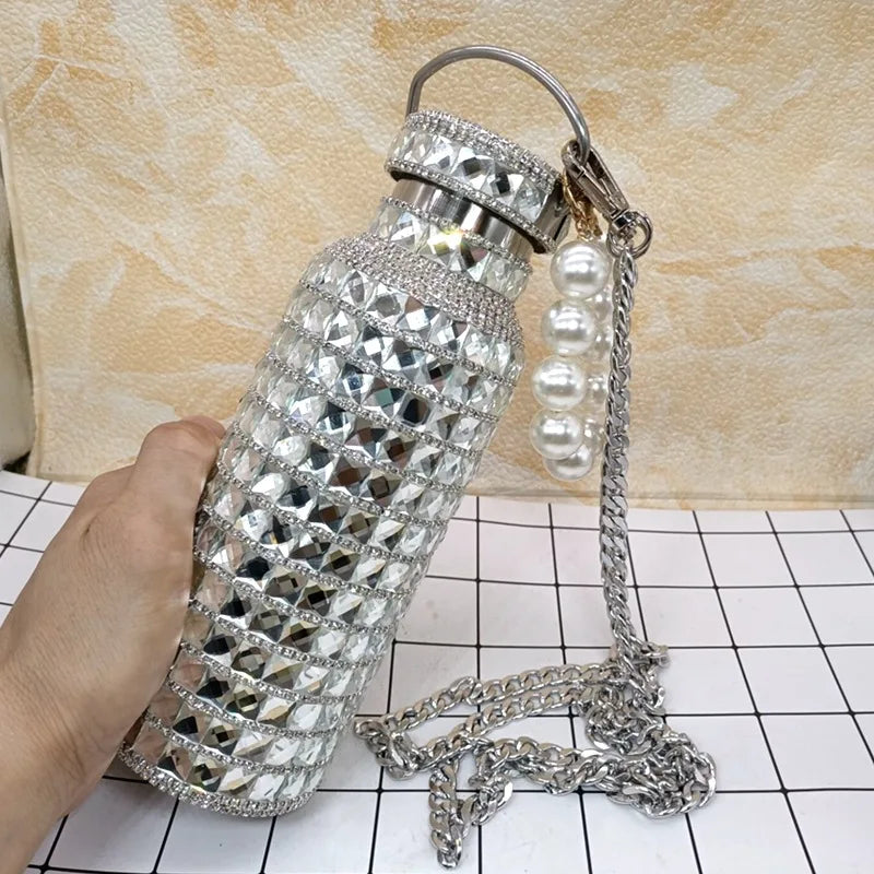 Decorative water bottle with rhinestone embellishments and a pearl-handled chain on a tiled surface.