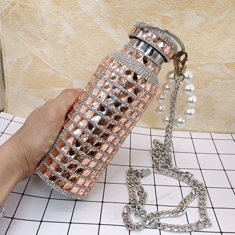 Rose gold water bottle with rhinestone detailing held by a hand on a checkered surface.