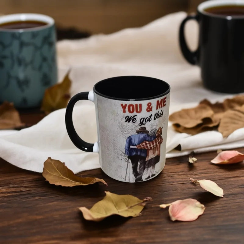Mug with 'You & Me, We got this' text and couple illustration on a wooden surface with coffee cups and leaves.