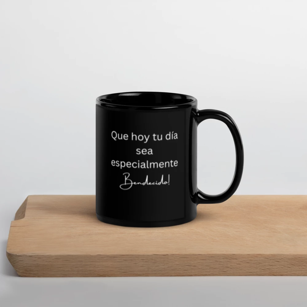 A black ceramic mug with white Spanish text reading 'Que hoy tu día especialmente bendecido!' sits on a light wood cutting board against a clean white background.