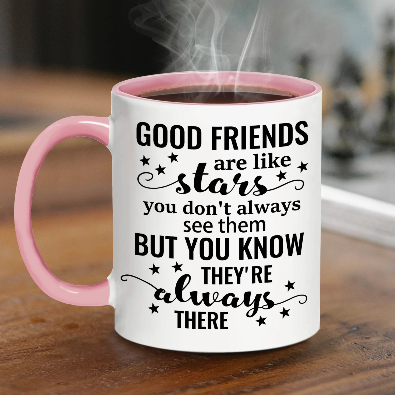 White mug with pink handle and coffee, featuring a motivational quote - GOOD FRIENDS ARE LIKE STARS... on a wooden surface.