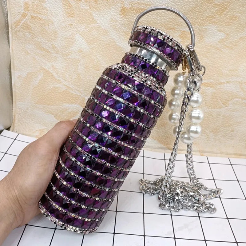 Decorative water bottle with purple gemstones and pearl chain on a checkered surface.