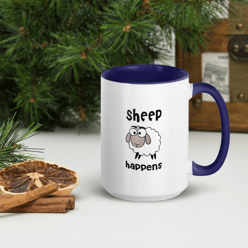 White mug with blue interior and handle featuring a cartoon sheep and 'Sheep happens' text, placed on a surface with decorative elements.