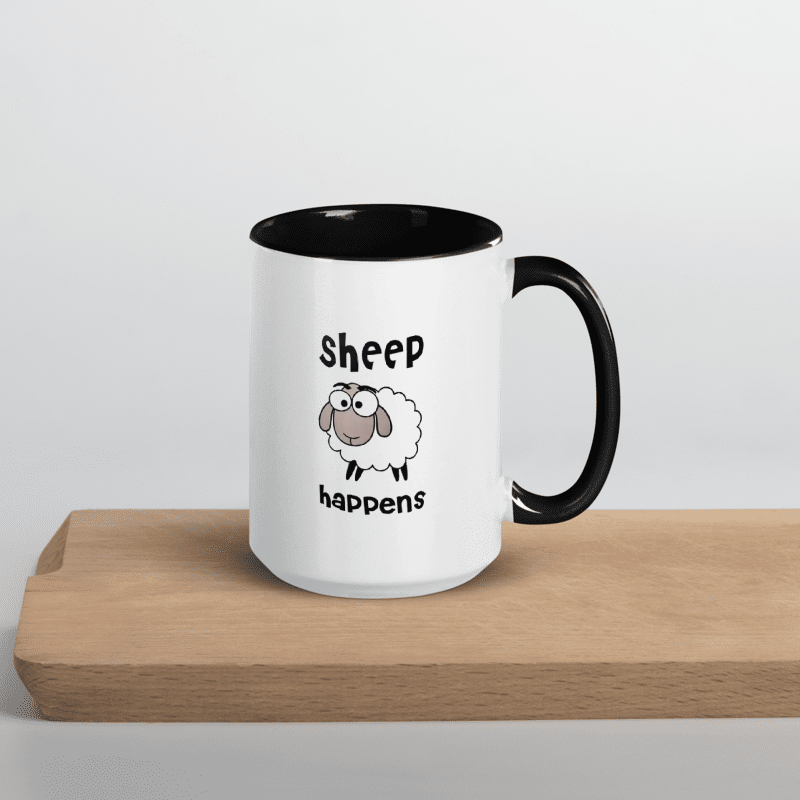 White mug with black handle featuring a cartoon sheep and 'Sheep happens' text on a wooden surface.
