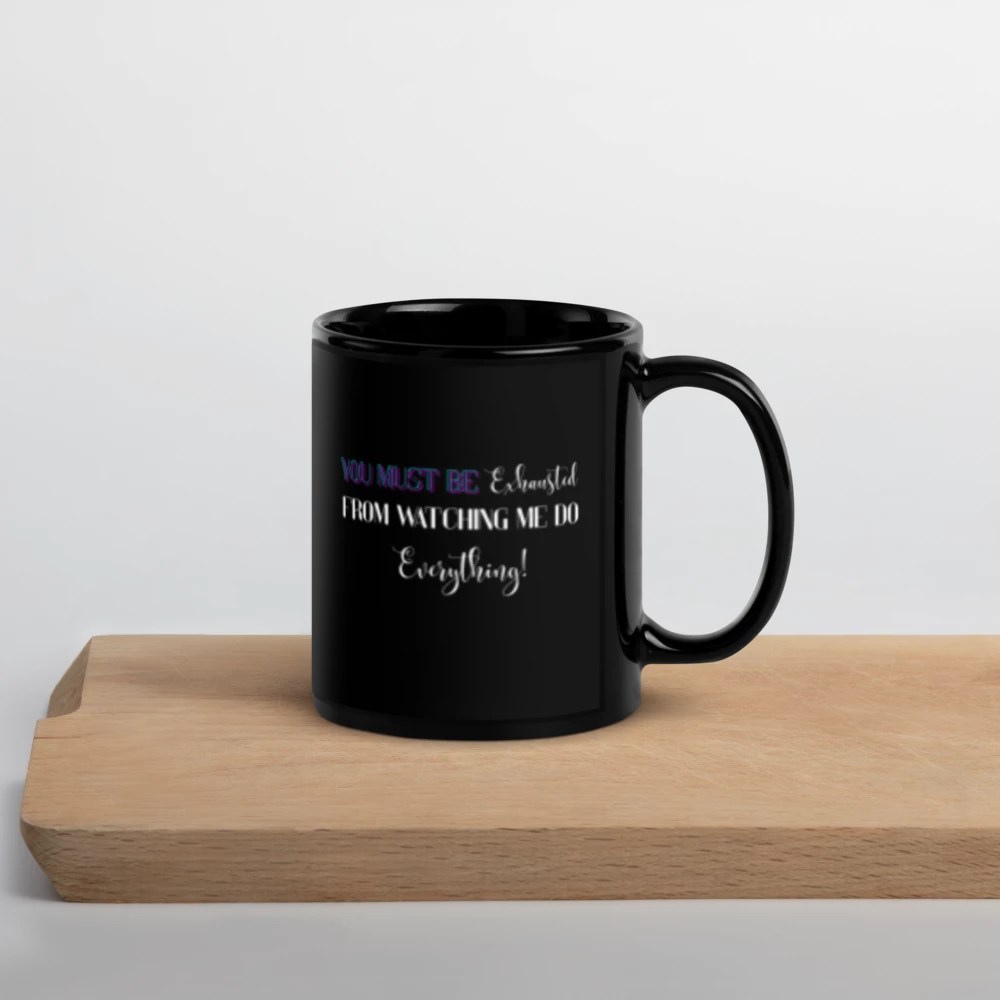 A black ceramic mug with a humorous quote printed on the front, resting on a light wooden cutting board against a clean white background.